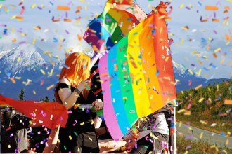 Composite image with pop singer Alaska with LGBT rainbow flag in background and Alaskan scenery in background.